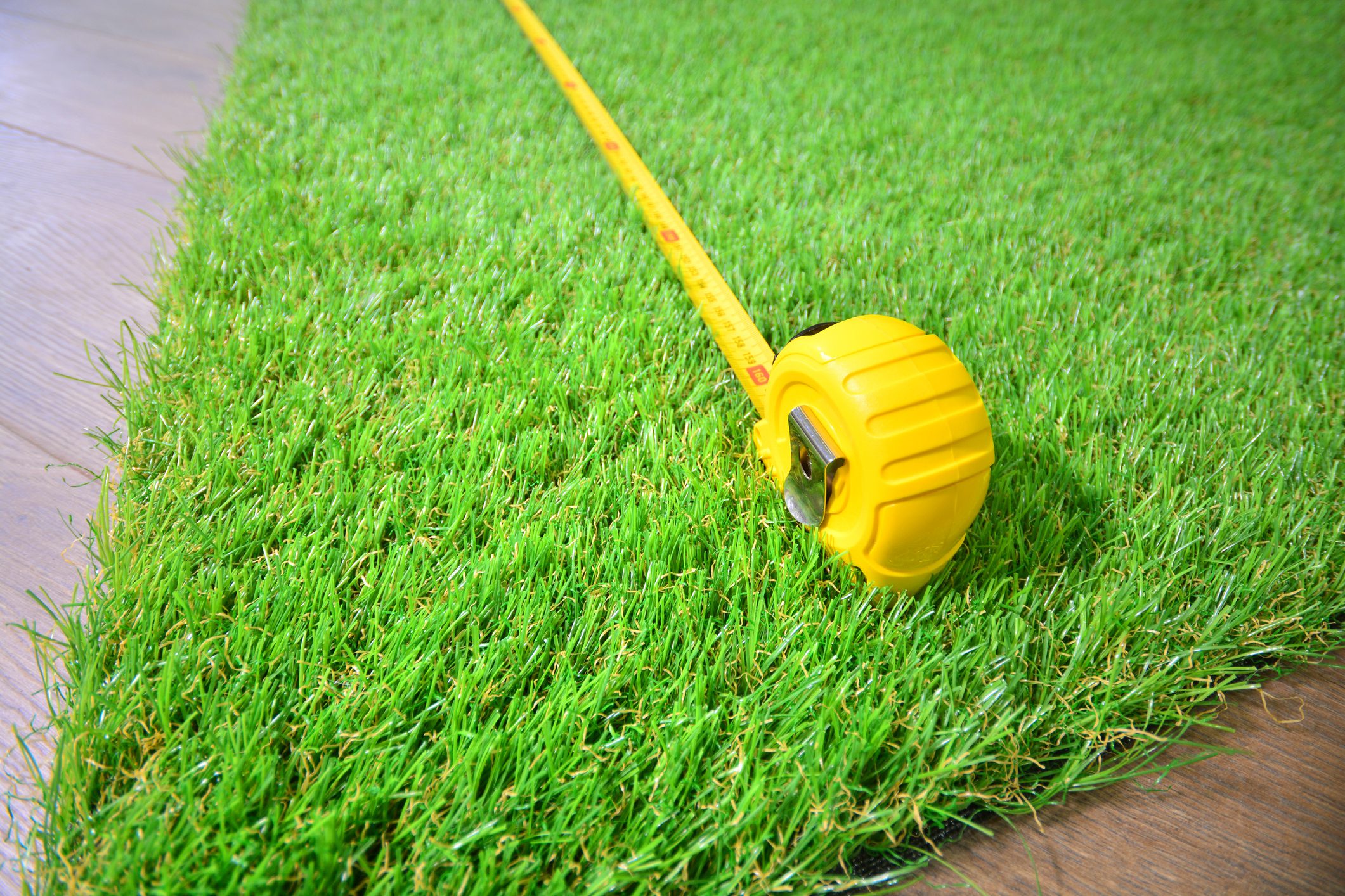 Artificial grass and measure tape lie on the laminate floor