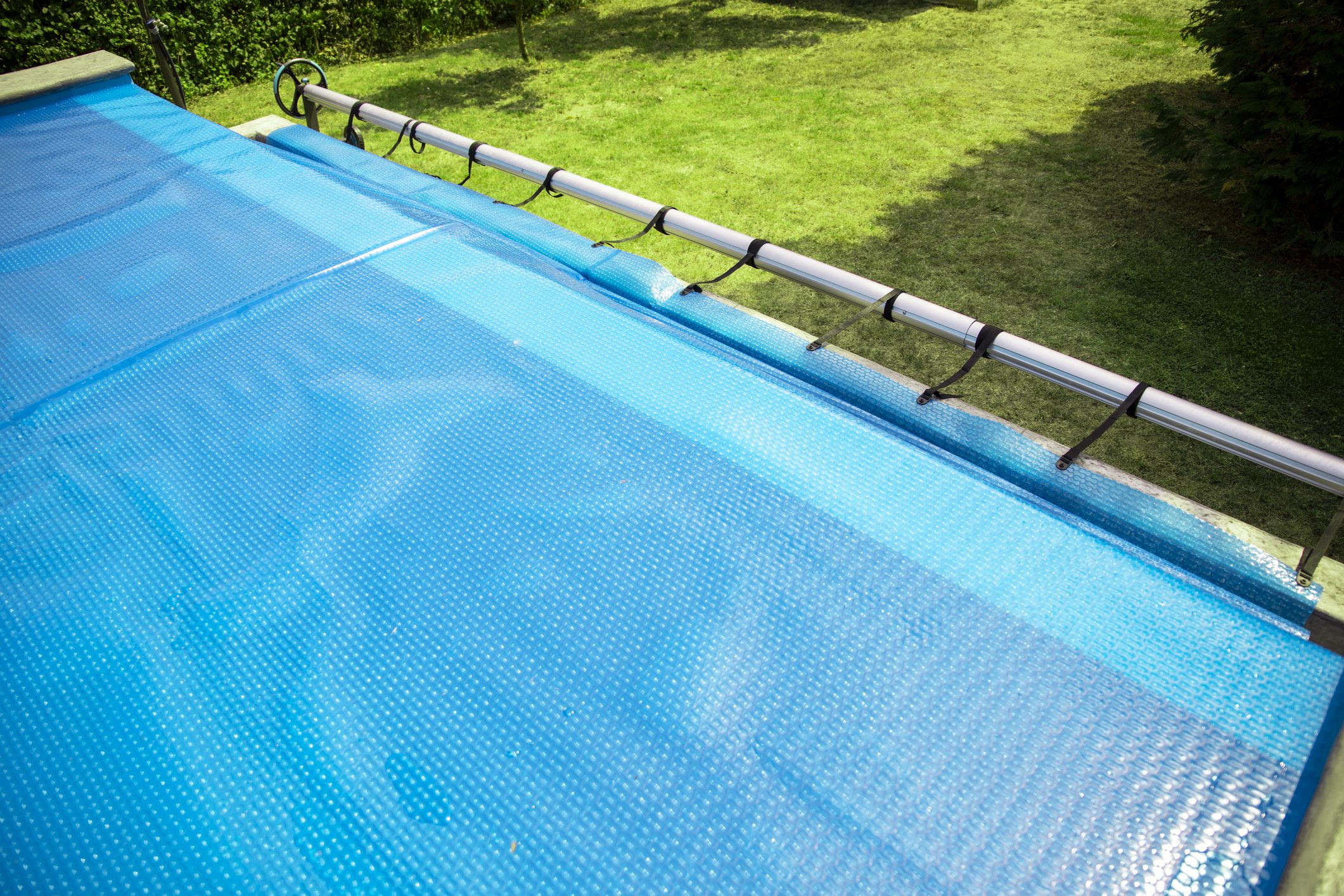 Part of blue solar pool cover floating on clean swimming pool. Keeping temperature and keeps clean the water