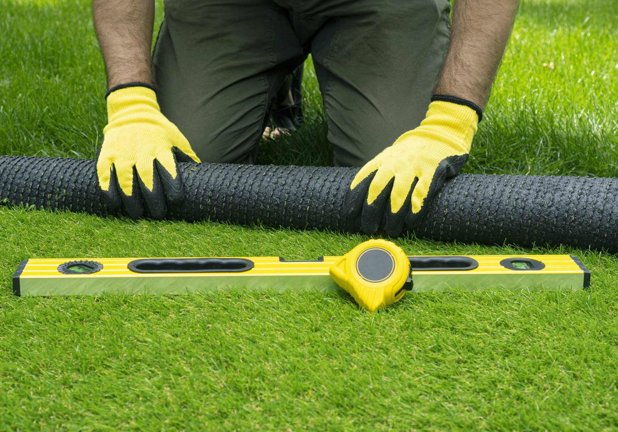 Landscaping of the yard with artificial turf. Male hands hold a roll of artificial grass.