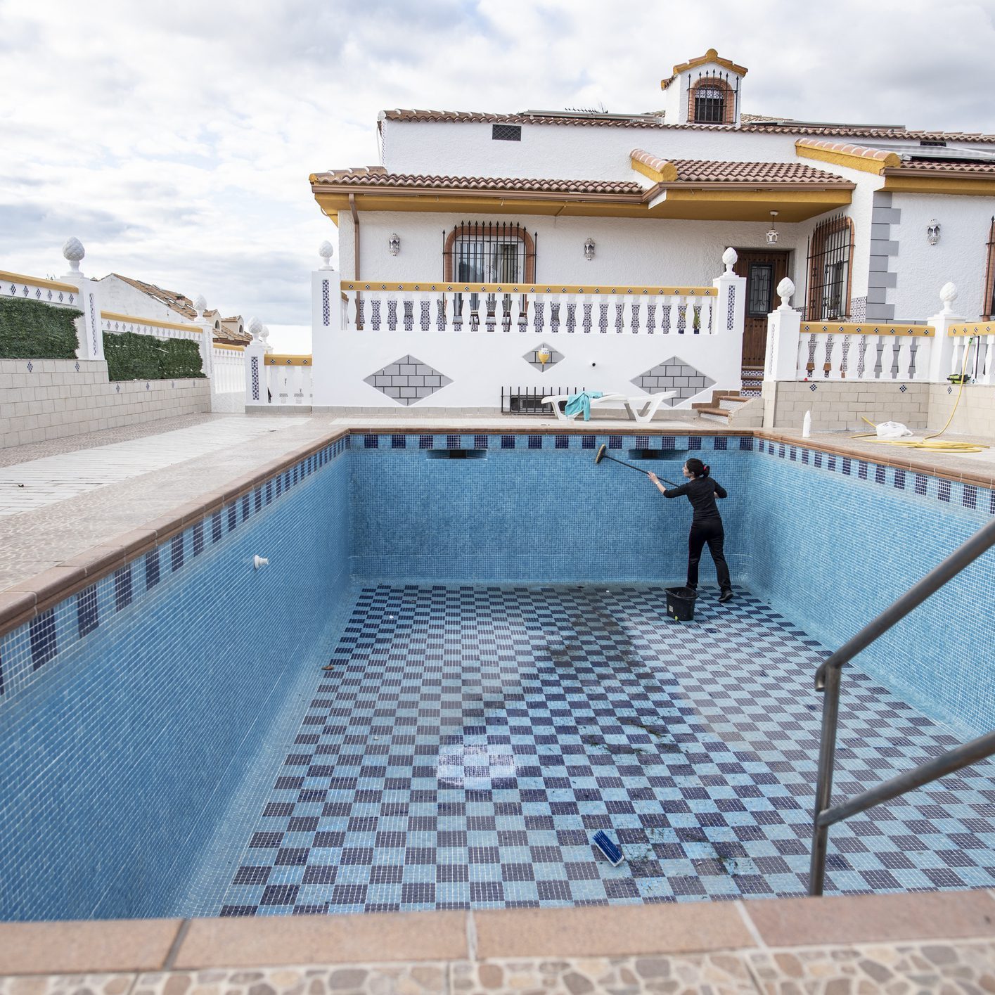 Person cleaning empty pool near house.