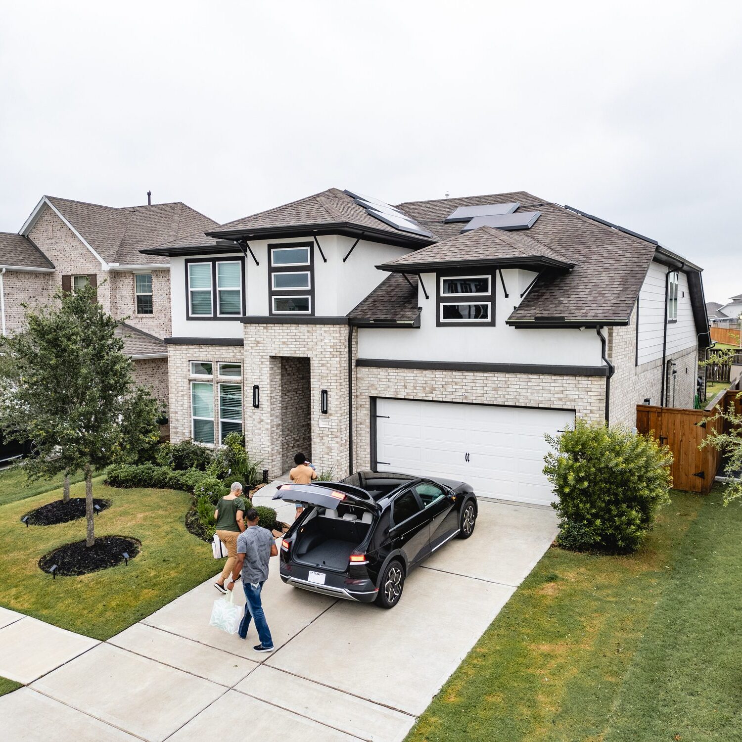 Family unloading car at suburban house driveway.