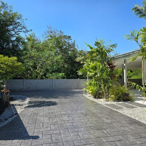 In Pattaya, Thailand, a stunning stamped concrete driveway showcases intricate designs. Lush plants and trees frame this serene outdoor space, a Thai Suburban area with a modern family house